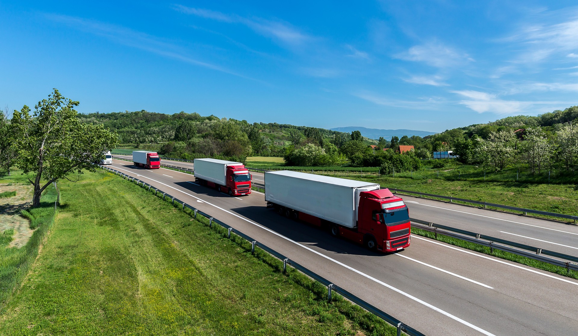 A convoy of trucks heading down the highway between meadows and dense forests.