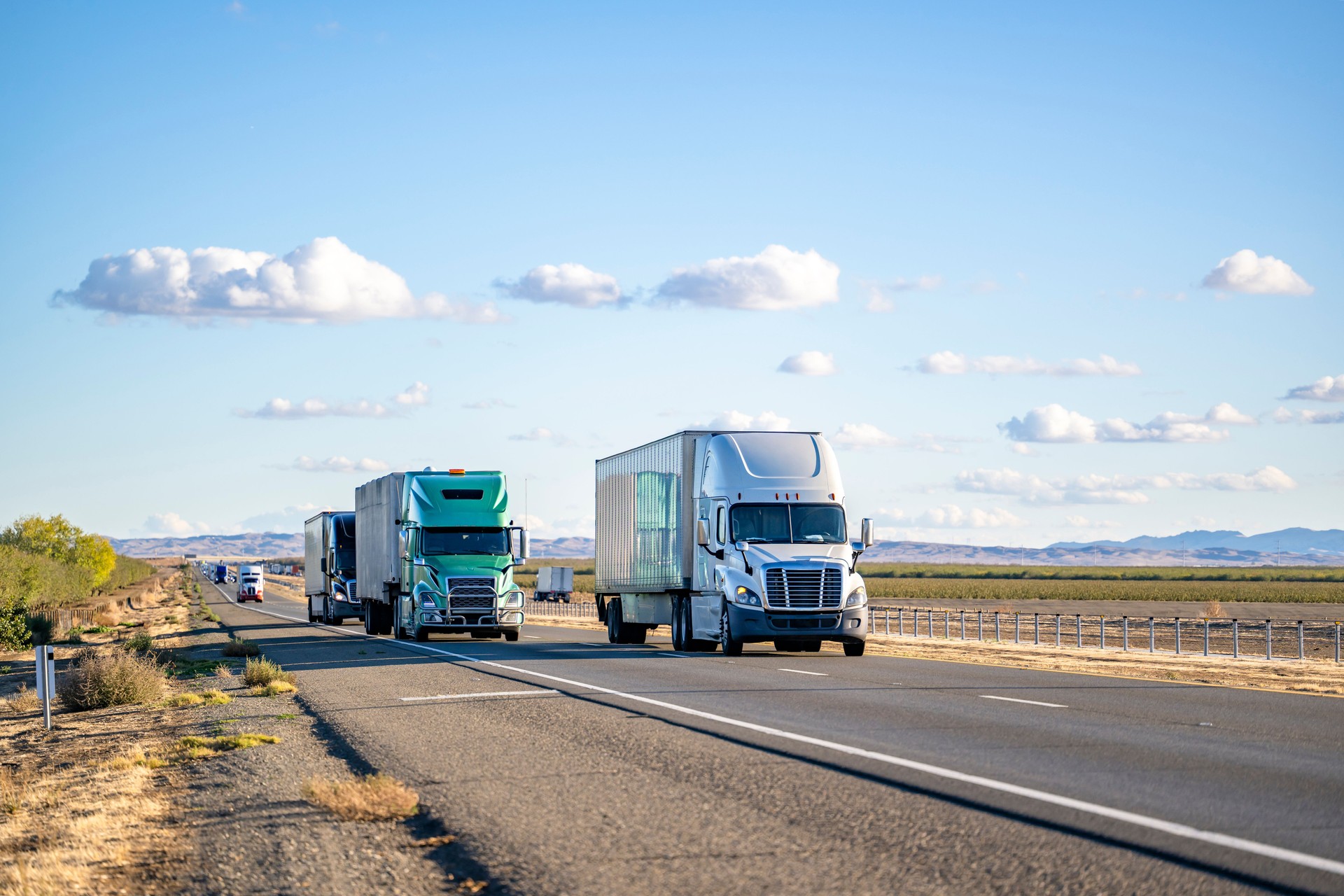 Convoy of the big rig semi trucks with different semi trailers carry cargo running on the divided highway road in both directions